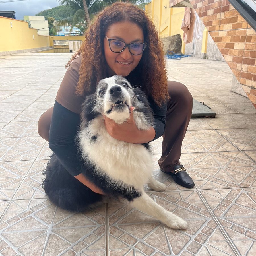 Dra. Mariana Helen agachada no nível do animal, abraçando um border collie após a consulta